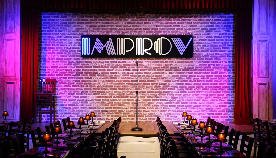Photo of the Improv stage lit in pink with empty tables and chairs in front at the Improv Comedy Theater & Restaurant. Orlando, Florida