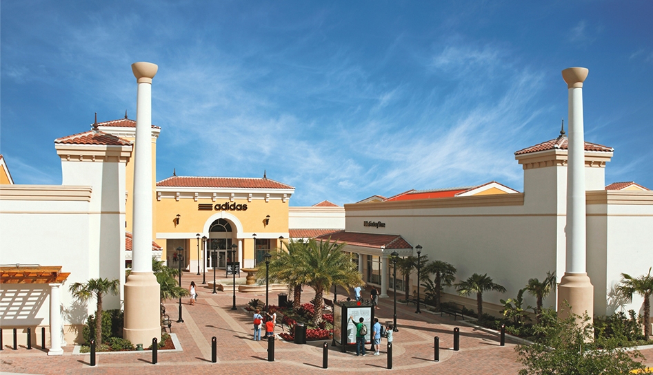 Daytime exterior photo of Orlando International Premium Outlets. Shoppers walking around entrance of Adidas. Orlando, Florida.