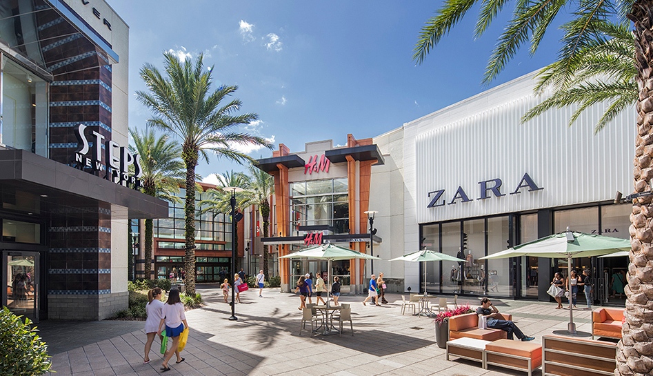 Daytime exterior shot of The Florida Mall. View of Steps New York, H&M, ZARA, and the mall entrance. Shoppers walking around outside. Orlando, Florida.