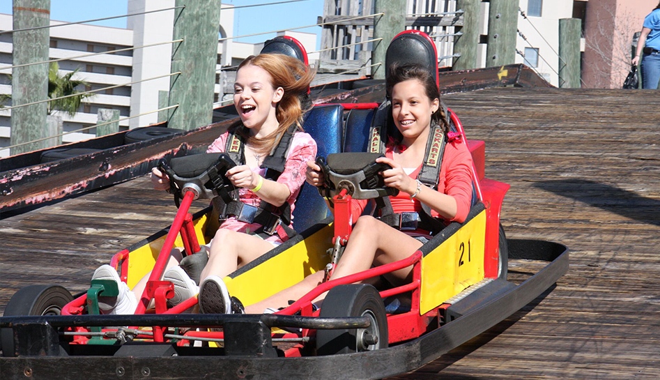 Two teen girls on a go-kart going downward on the track at Magical Midway Thrill Park. Daytime photo. Orlando, Florida.