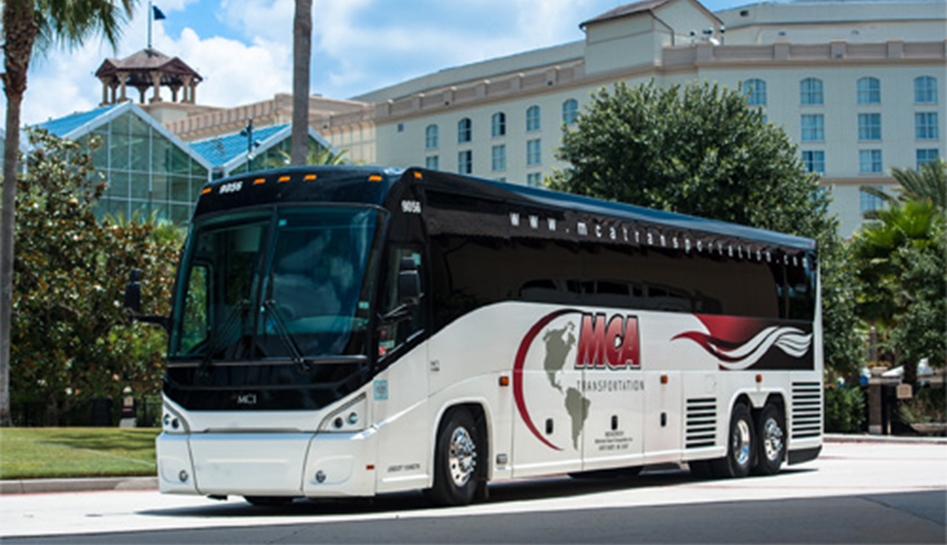 An MCA charter bus parked outside of a hotel during the daytime. MCA Transportation. Orlando, Florida.