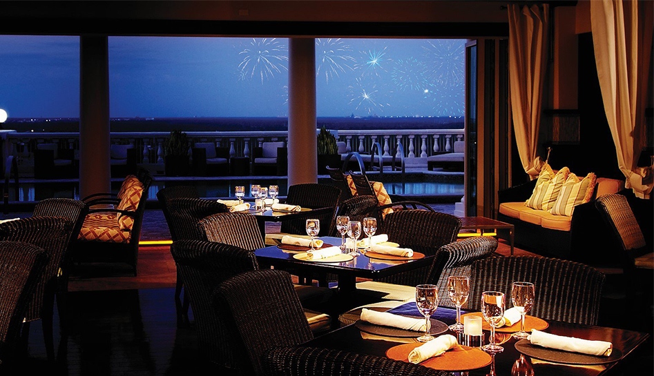 Evening photo inside of Eleven restaurant. Tables are set and the windows show a dim blue sky with fireworks in the distance. Reunion Resort. Kissimmee, Florida.