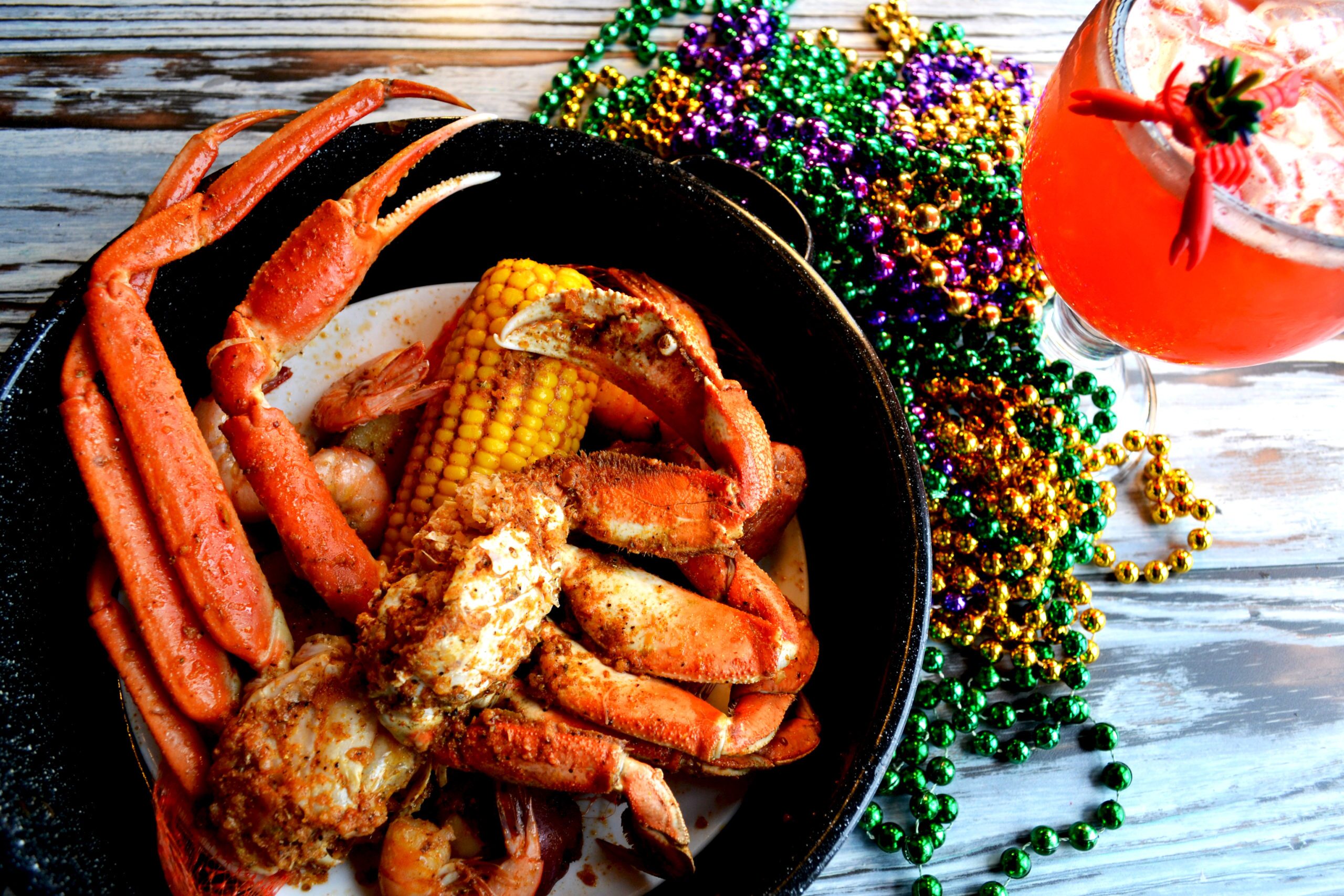Photo of crab leg entree with a drink to the right and mardi gras beads surrounding the dish. Joe's Crab Shack. Kissimmee, Florida.