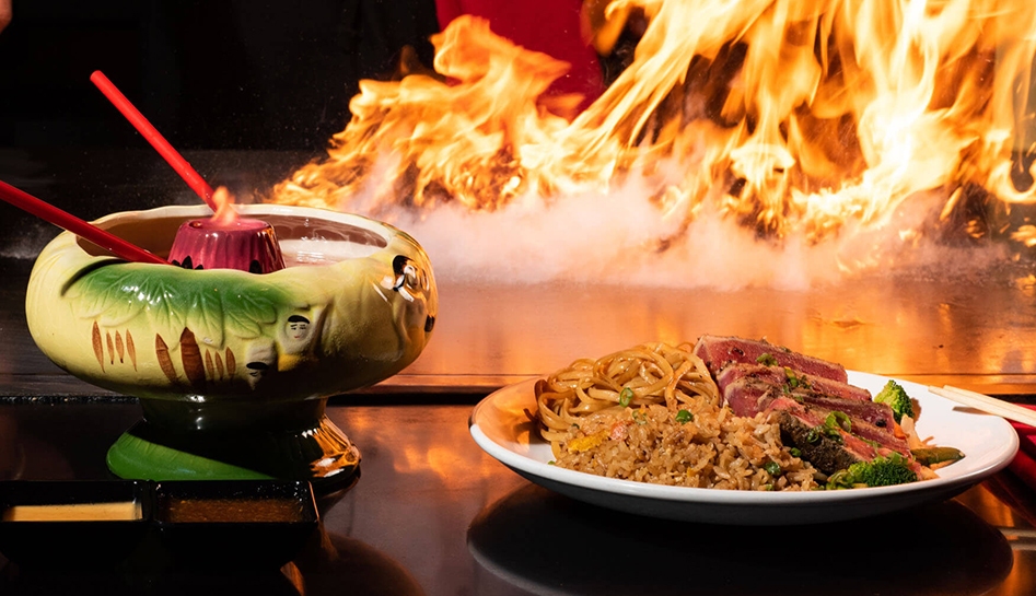 Green drink bowl (left) and hibachi plate (right) with fire in the background. Kobe Japanese Steakhouse. Kissimmee, Florida.