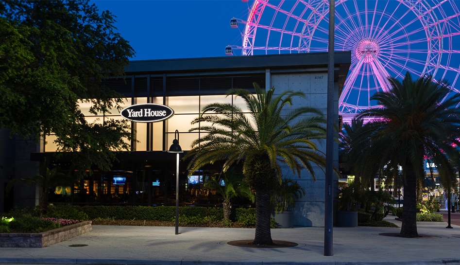 Evening photo of the front of Yard House restaurant (left) with ICON Park ferris wheel lit in pink in the background (right). Orlando, Florida.